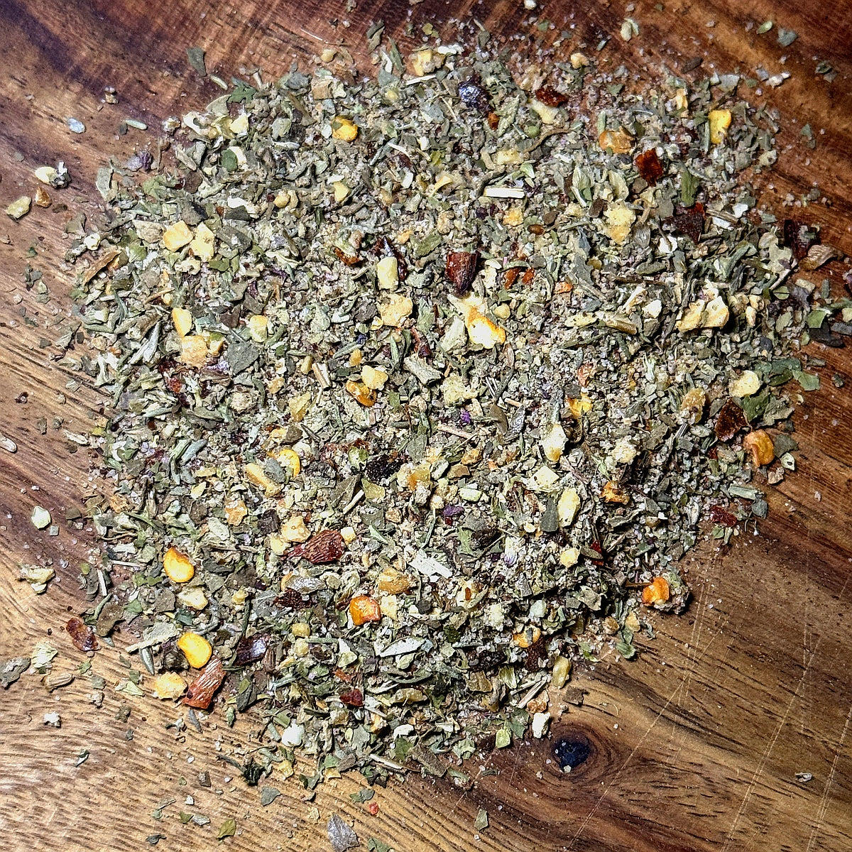 Tangy Herb Seasoning - Tuscan Evening, a vibrant mix of herbs and spices on a wooden surface.