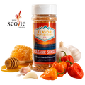 A bottle of Flavor Expedition Co. 'Volcanic Sunset' seasoning stands on a white background surrounded by food props including honeycomb, honey, a honey dipper, garlic cloves, red and orange habanero peppers, and chili peppers. [pack-1]