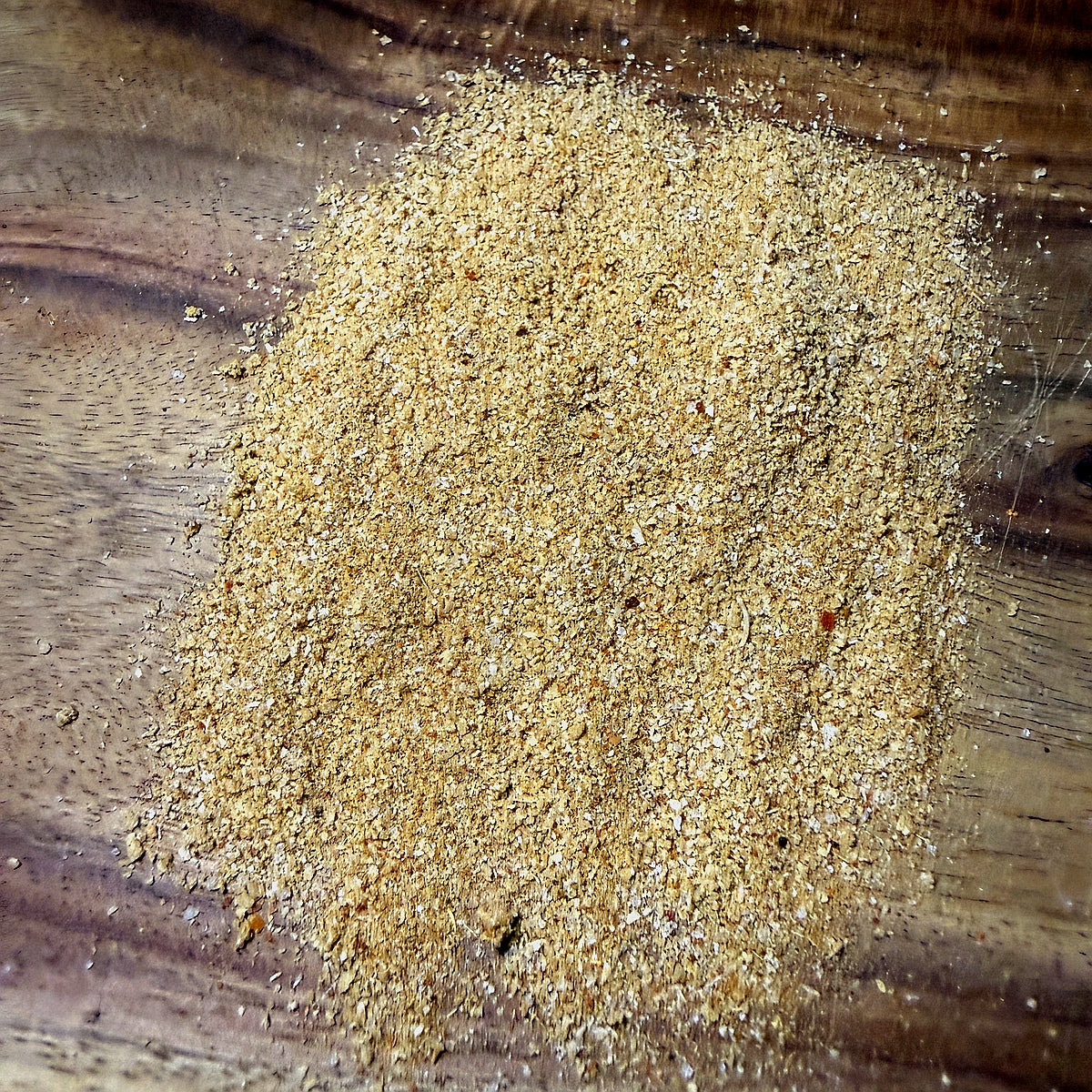 Green Chile Chipotle Seasoning powder spread on a wooden surface, showcasing its rich texture and color.