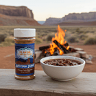 Green Chile Chipotle Seasoning by Western Dawn next to a bowl of chili by a campfire in nature.