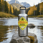 Season Recklessly Sticker on a stylish water bottle by a serene river in the mountains, showcasing weatherproof durability.