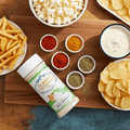 Snack platter with popcorn, chips, fries, and a bottle of seasoning on a wooden board.